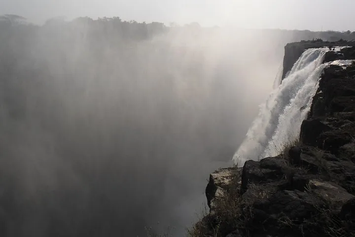 Ein nebliger Blick auf die Victoriafälle, die über eine steile Felswand stürzen.