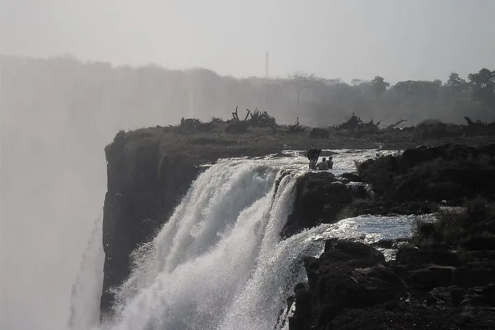 Eine Weitwinkelaufnahme der Victoriafälle mit dichtem Gischtnebel und Wasser, das über die Kante fließt.